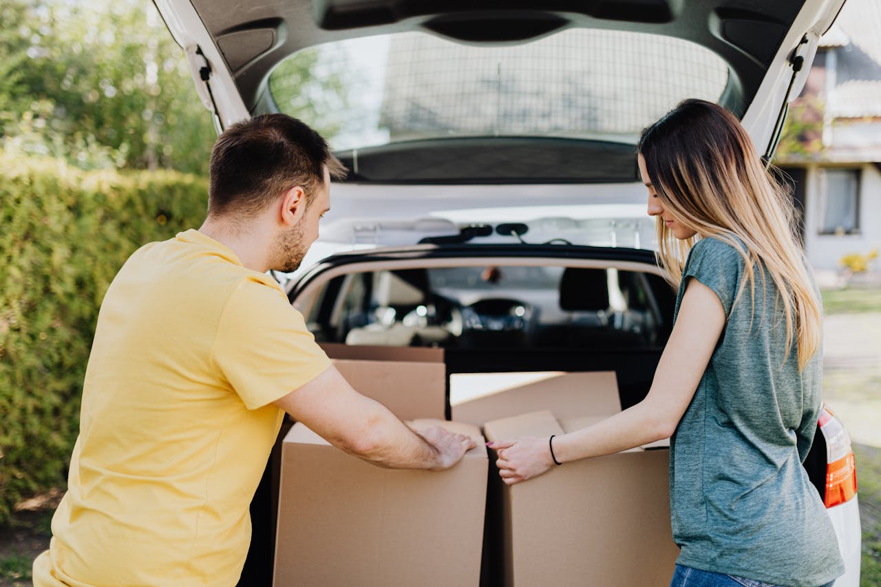 A couple loading cardboard boxes into a car trunk for moving day.